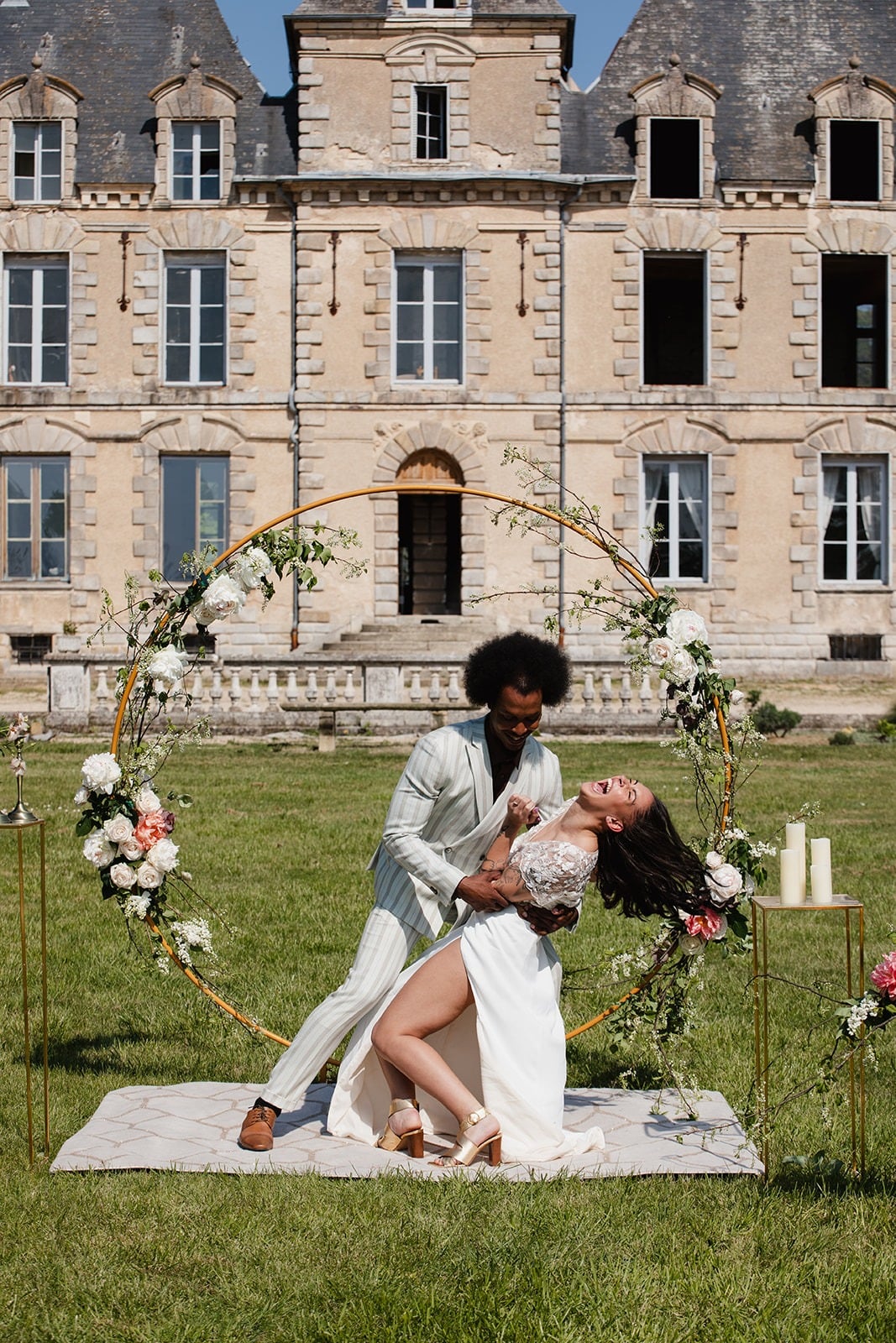 cérémonie de mariage devant un chateau ave cun couple de mariés devant une arche rose en cuivre